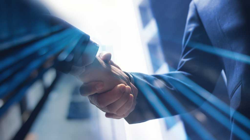 A low-angle photograph of two people in business suits shaking hands.